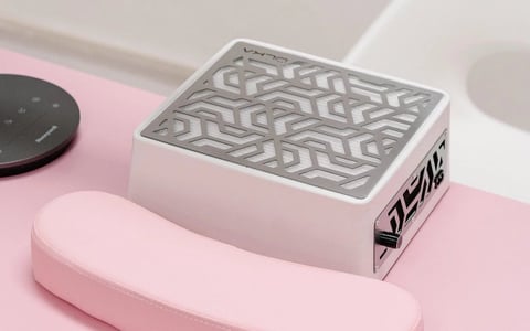 White rectangular device with geometric patterned top display on pink and white surfaces, surrounded by modern tech accessories