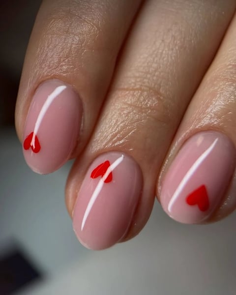 Close-up of manicured nails with soft pink polish and small red heart accents on three visible nails