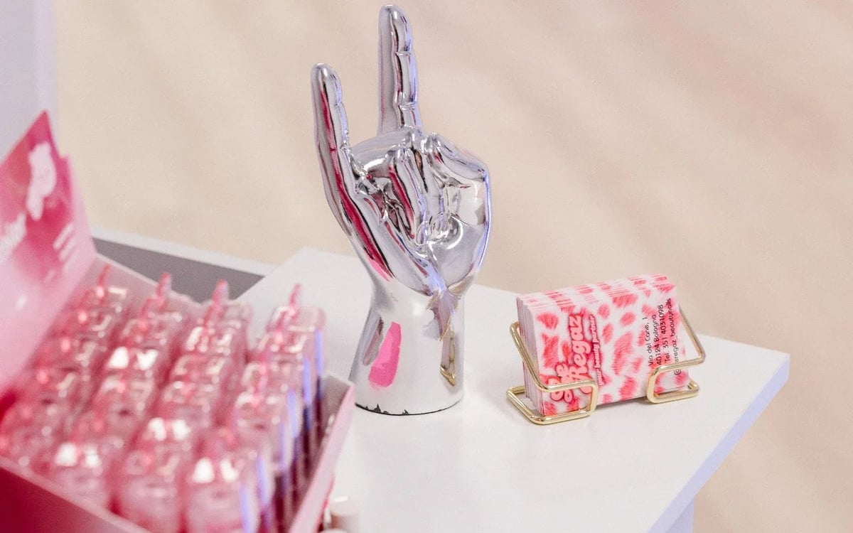Clear crystal hand sculpture displayed on white platform with pink decorative items in background