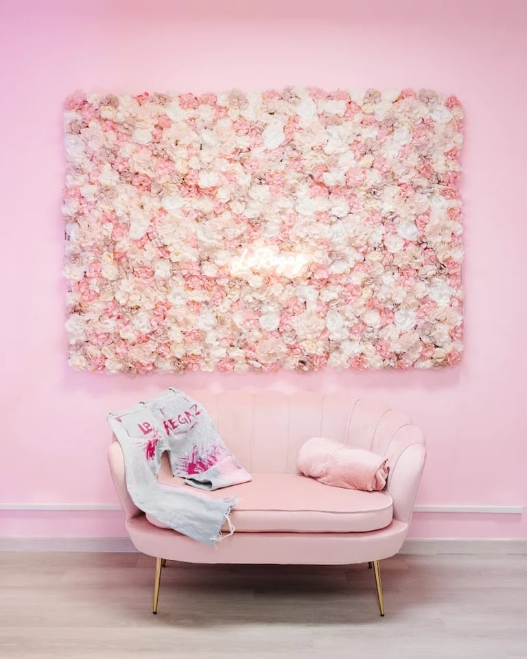 Pink and white floral wall backdrop above a modern pink chair with magazines and a pillow in a styled interior space