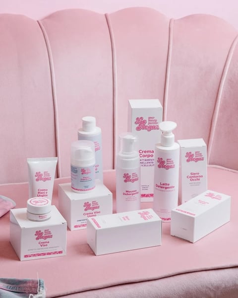 Collection of pink and white skincare and cosmetic products displayed on white blocks against a pink fabric backdrop