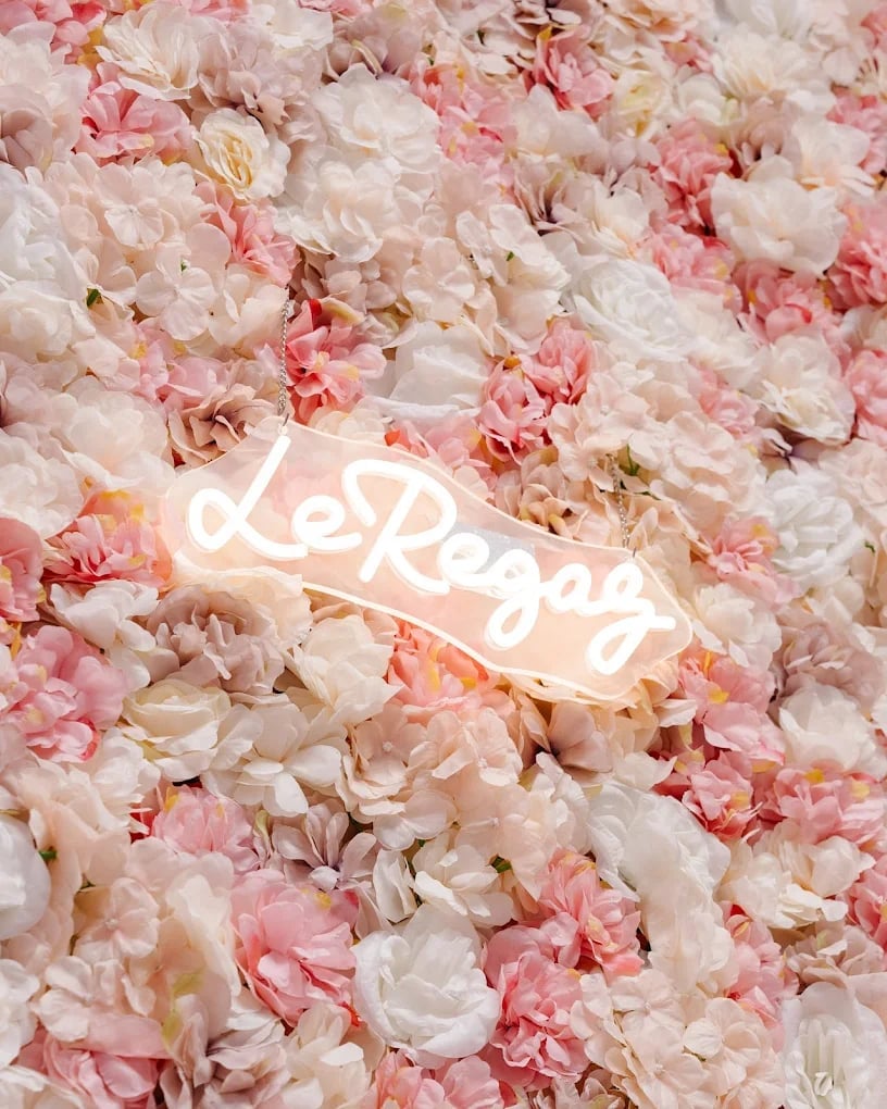 Neon love sign glowing white against a lush backdrop of pink and cream carnation flowers