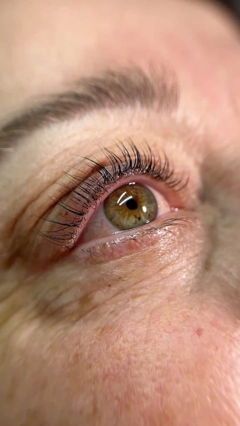 Close-up of a woman's eye with full black lashes and hazel iris showing detailed makeup application