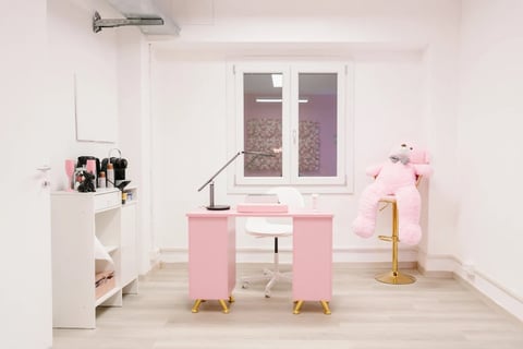 Modern minimalist bedroom with pink desk, white shelving, desk lamp, and gold accents. Large window with purple curtains overlooks outdoor scenery